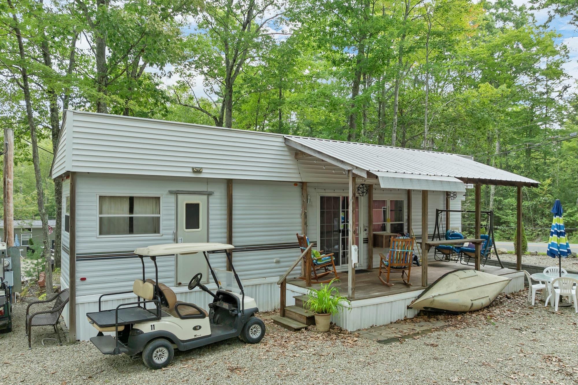 The white park model from the site, with the covered deck, a golf cart, and a kayak